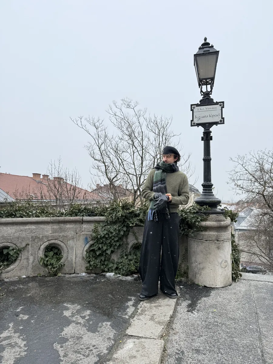 Jan mit Baskenmütze, Schal und weiter Hose an einer Laterne