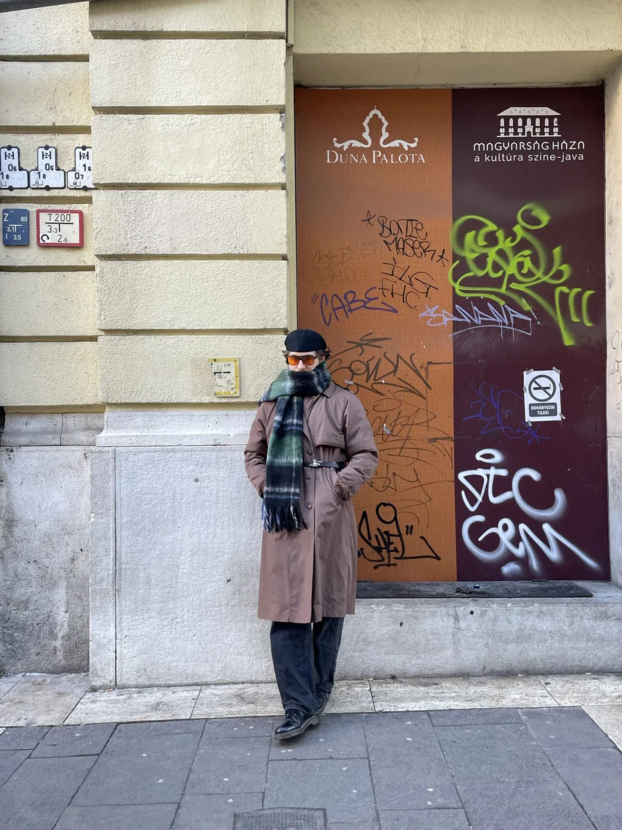 Jan im Trenchcoat mit Schal vor einer Wand mit Graffiti